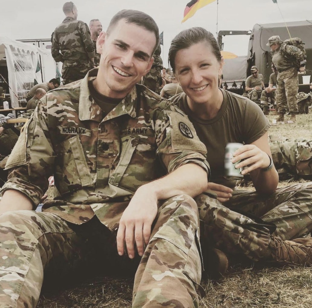 Regan Kulhavy and her husband sitting together in military uniforms at a field camp