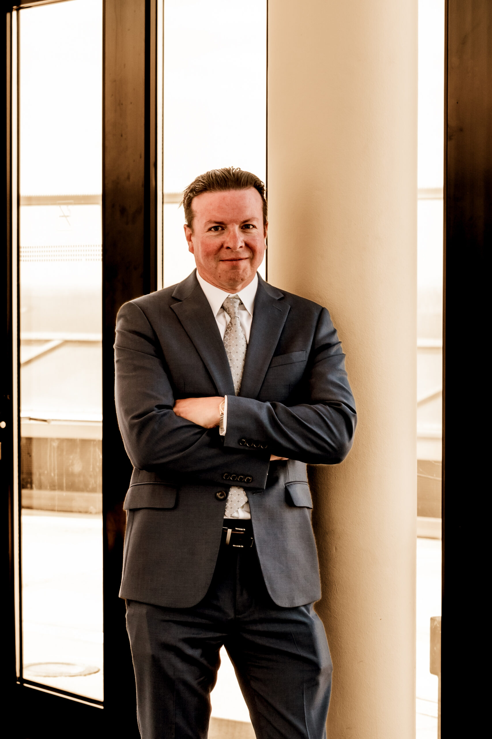 Andre Le Blanc in navy suit standing with arms crossed by column