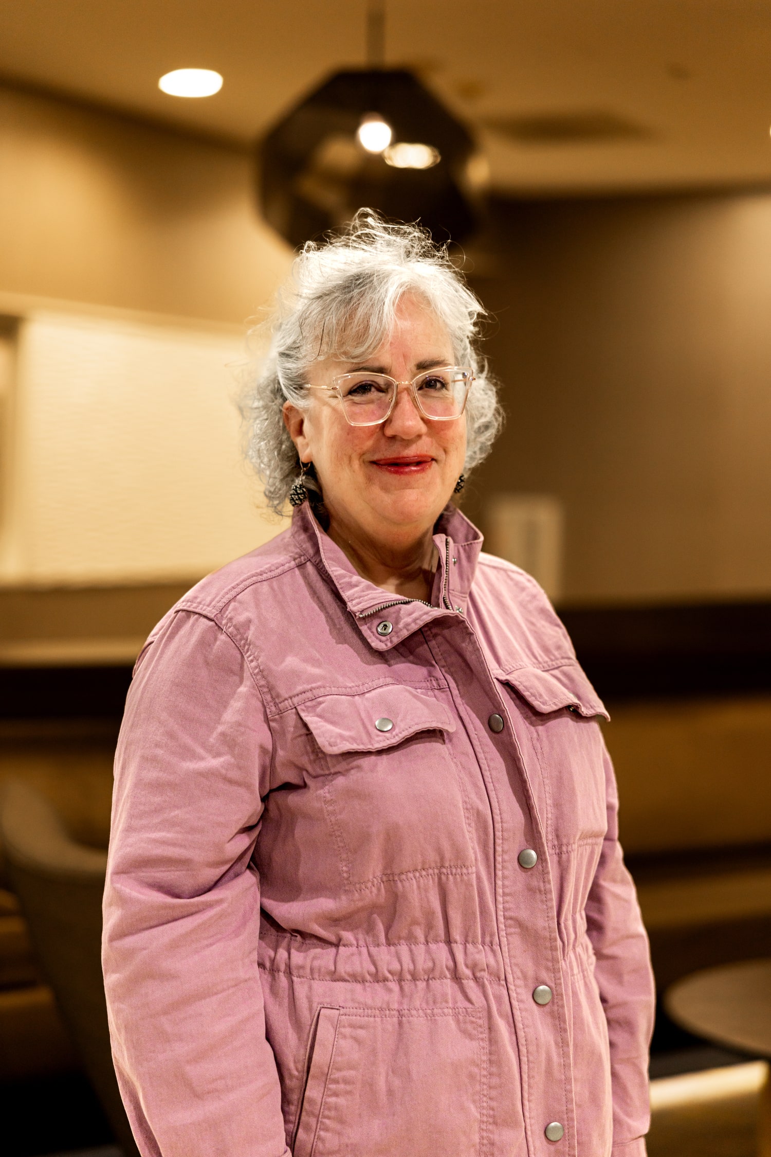 Genie Hughes standing in a pink jacket in a warmly lit room