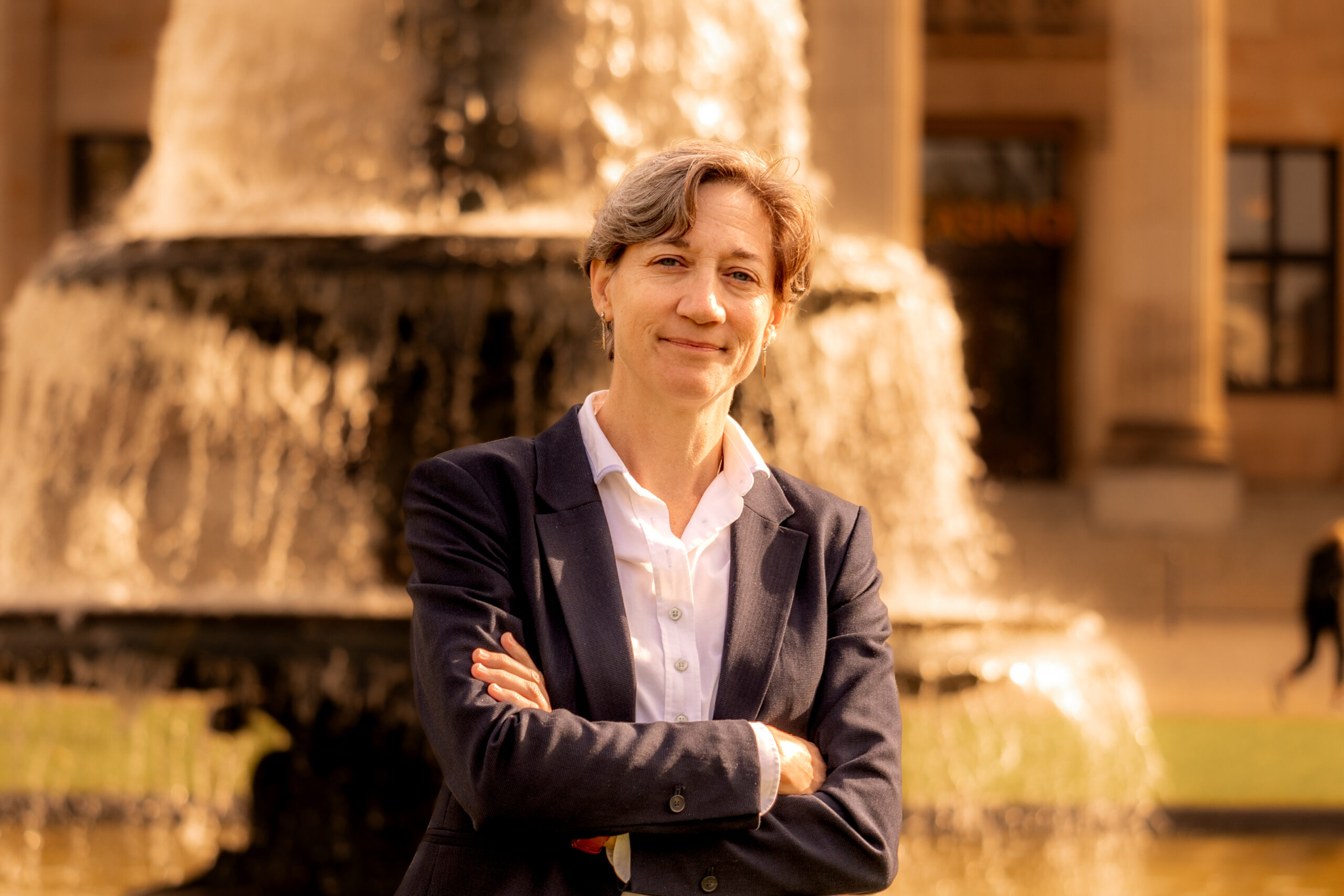 Mary Ritzmann smiling with arms crossed in front of a large fountain