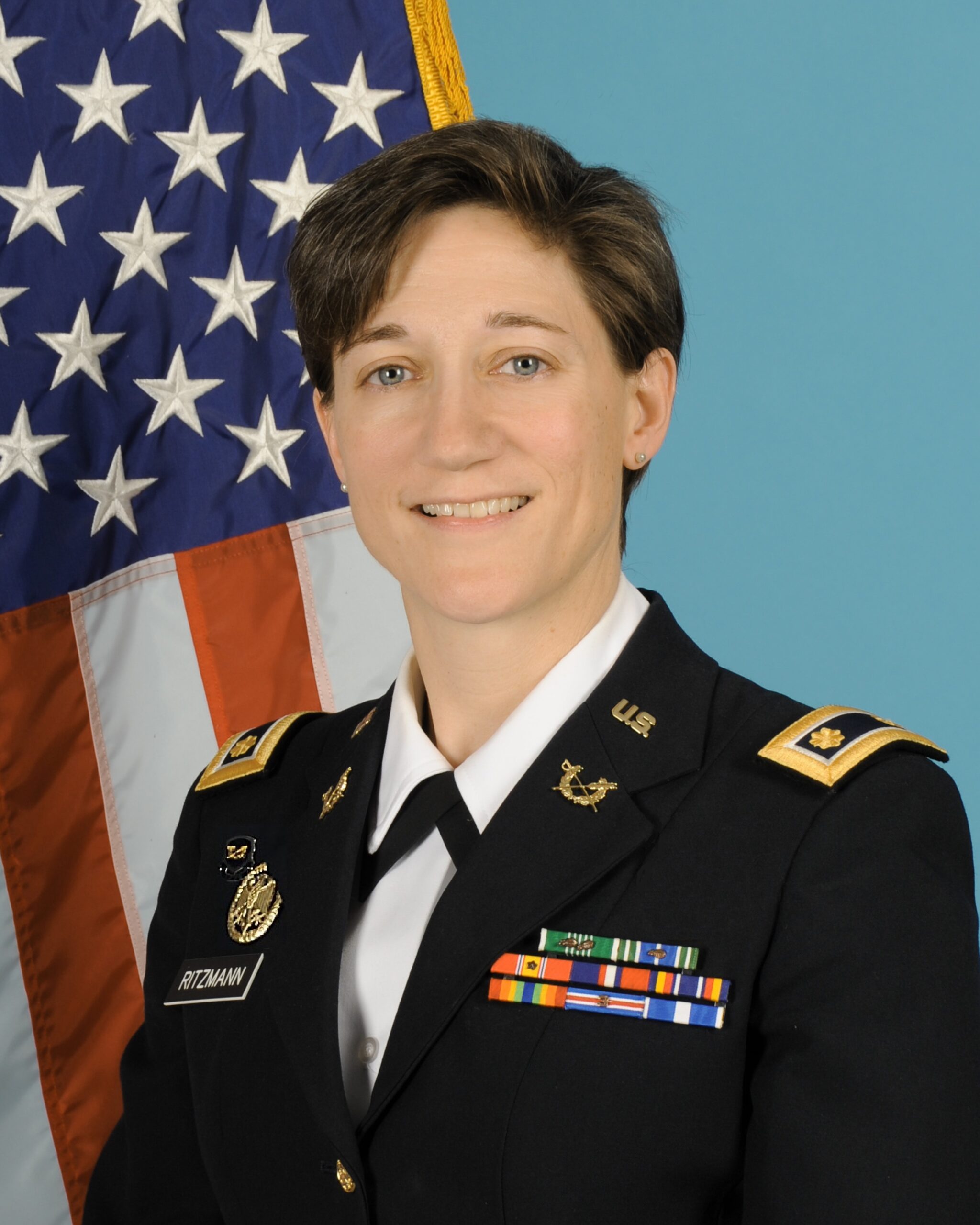 Mary Ritzmann in Major Army Service Uniform standing in front of the American flag