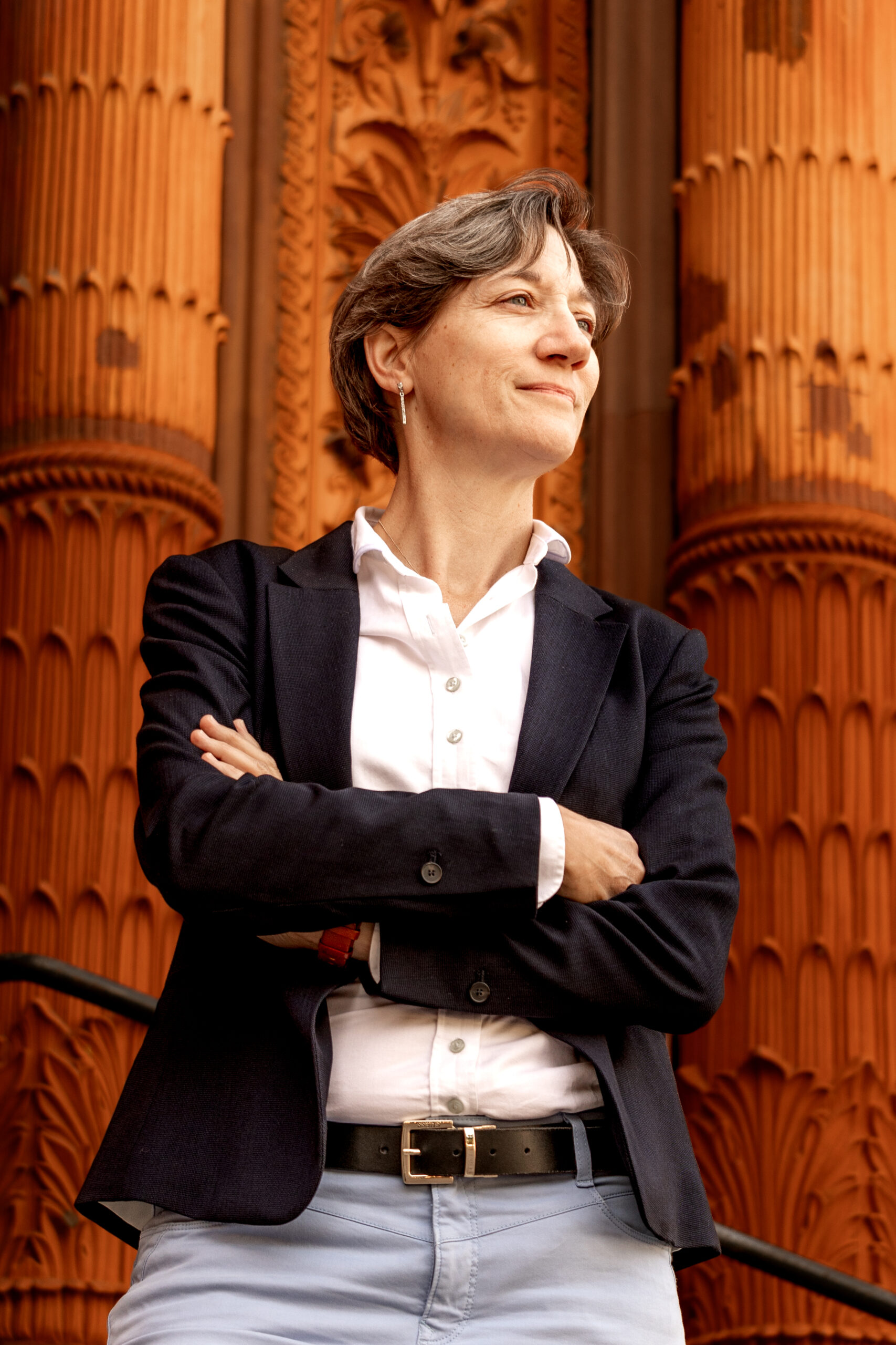Mary Ritzmann in blazer looking upwards with wooden columns in the background