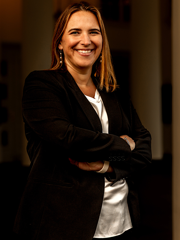Elizabeth Talarico Elizabeth Talarico in a black suit and white blouse, standing with arms crossed in a hallway