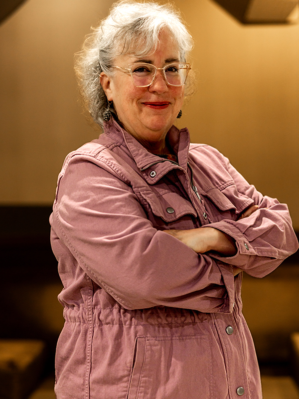 Genie Hughes Military attorney Genie Hughes standing with arms crossed, wearing pink jacket indoors
