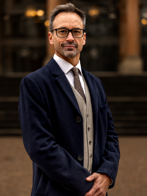 John Caulwell Military attorney John Caulwell standing with hands clasped, wearing navy blazer and patterned tie