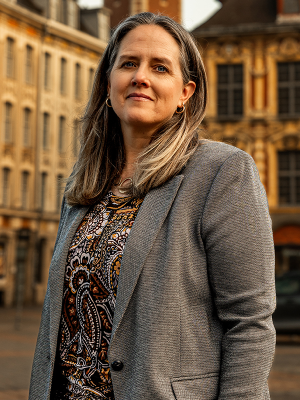Kyle Meisner Military attorney Kyle Meisner standing outdoors, wearing patterned blouse and grey blazer with buildings in the background