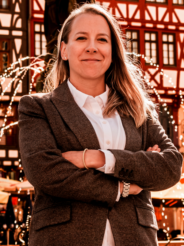 Natalia Helmsing Military attorney Natalia Helmsing standing outdoors, wearing brown plaid blazer and white shirt with arms crossed