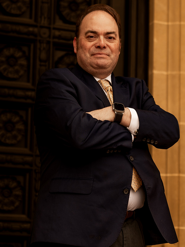 Robert Newark Military attorney Robert Newark standing outdoors, arms crossed, wearing navy suit and yellow patterned tie