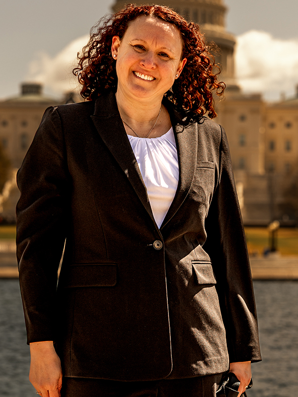 Victoria Camire Military attorney Victoria Camire standing outdoors in front of a government building, wearing black suit and white blouse