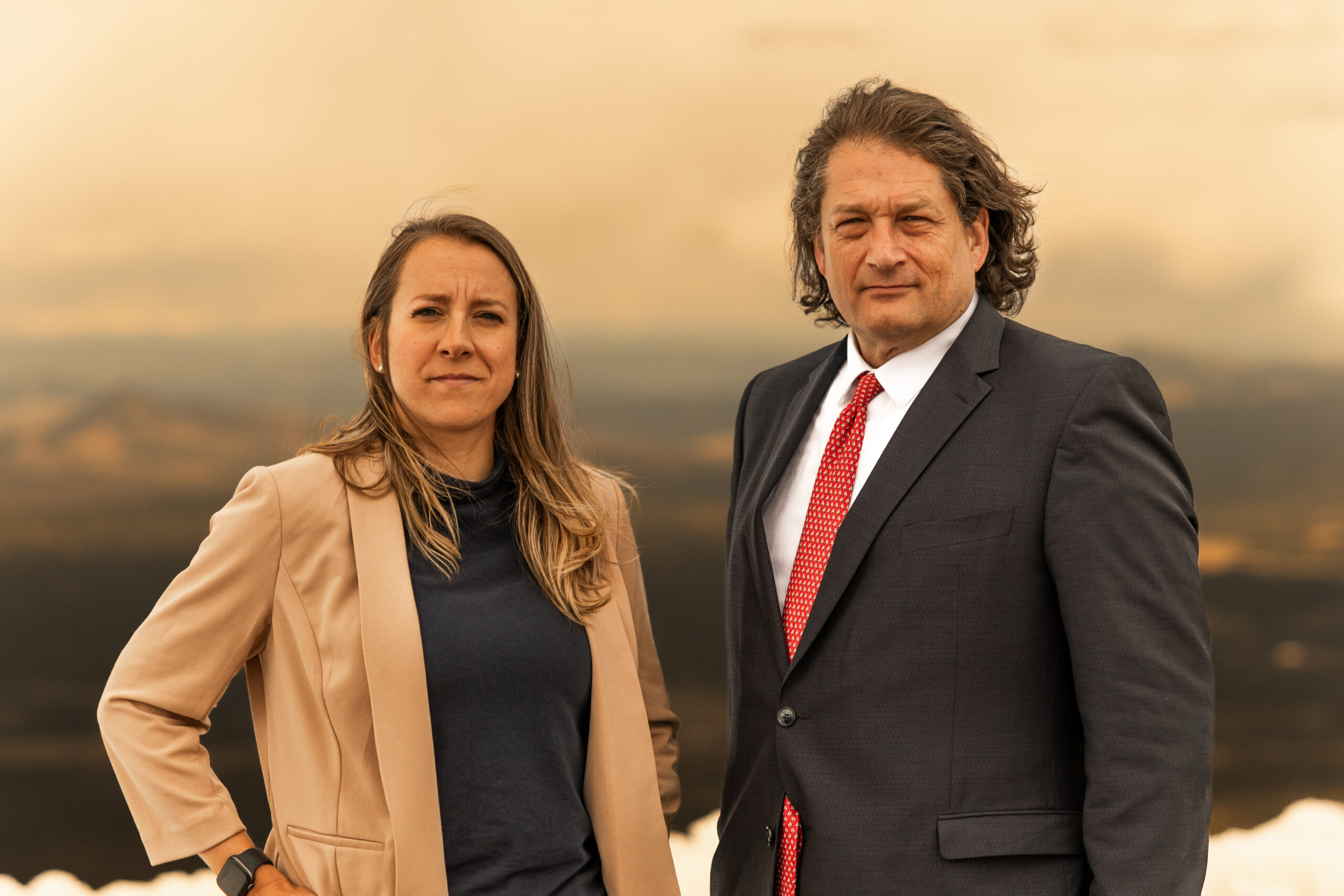 Natalia Helmsing and Will M Helixon standing outdoors in business attire with scenic background