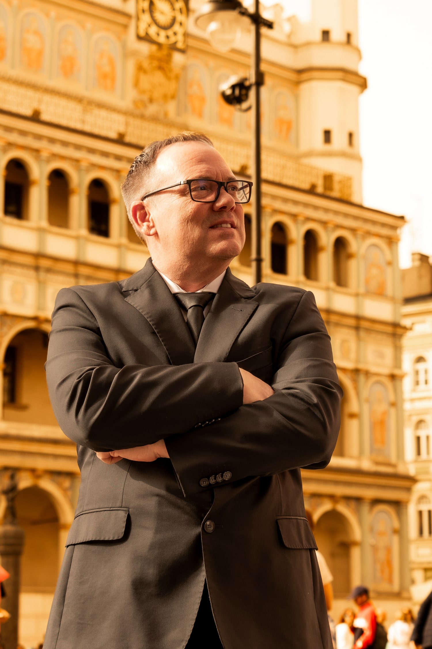 Scott Brokaw in a black suit with arms crossed standing in front of a historic building