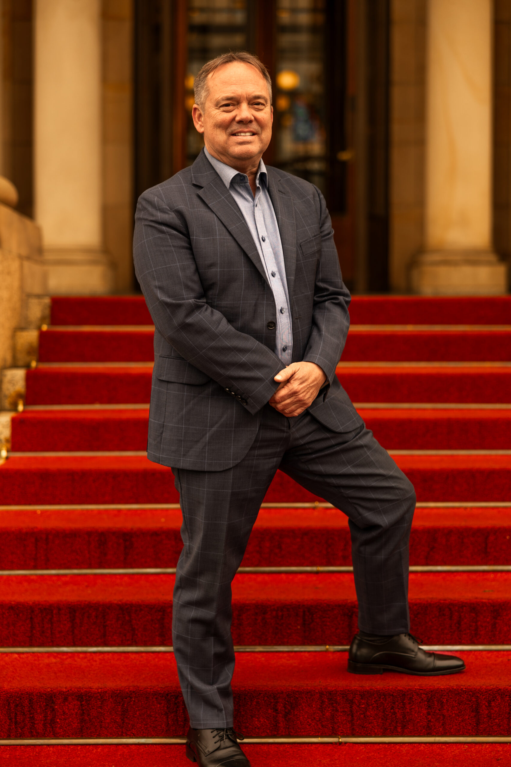 Scott Brokaw standing and smiling on red carpeted stairs