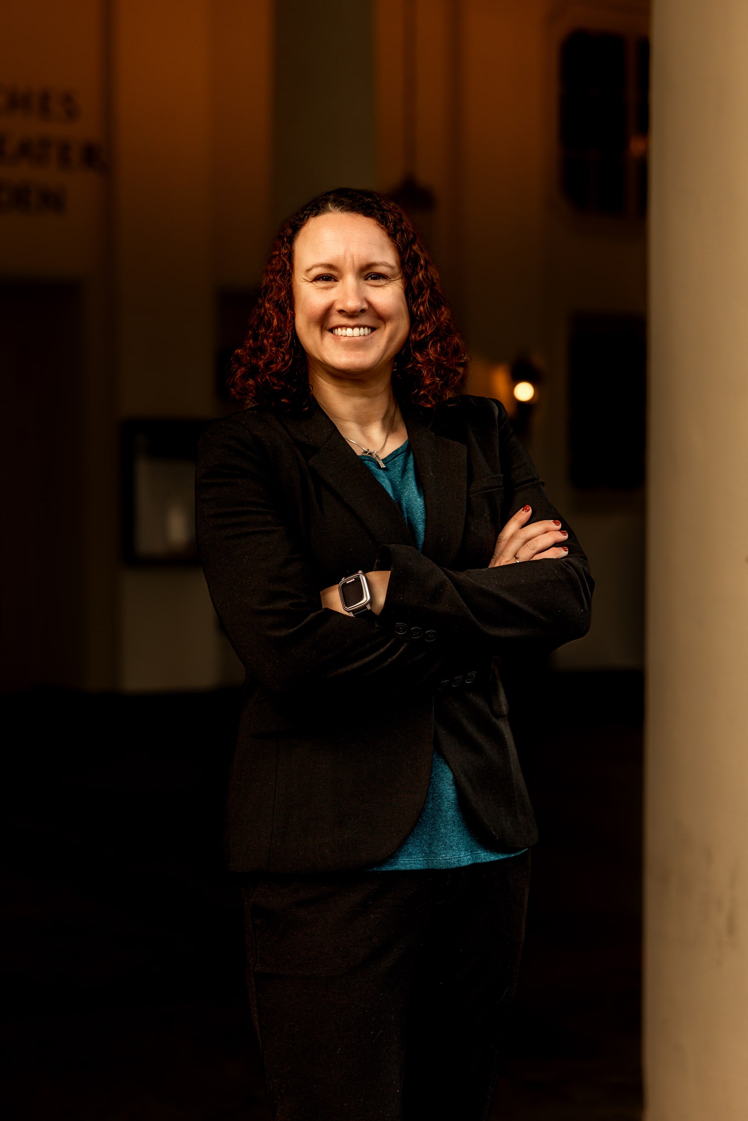 Victoria Camire in professional attire, standing with arms crossed inside a softly lit hallway