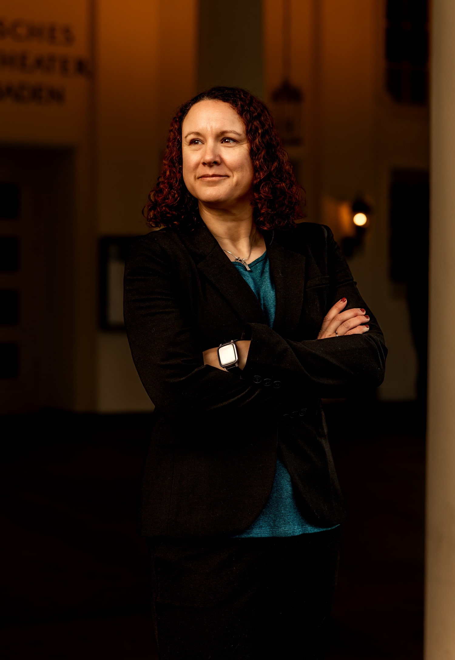 Victoria Camire in business attire, arms crossed, standing in a hallway and gazing away from the camera