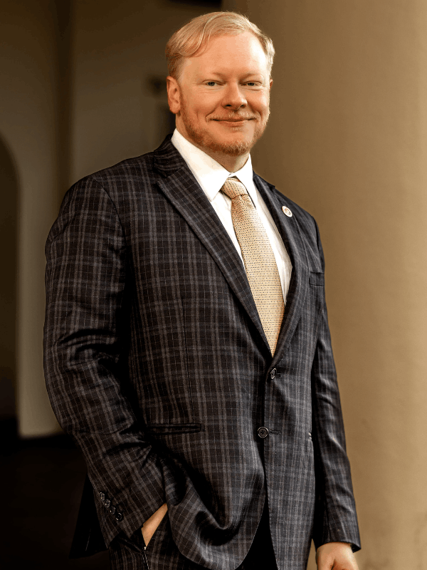 Cadman R. Kiker, military defense attorney, smiling in a plaid suit and gold tie