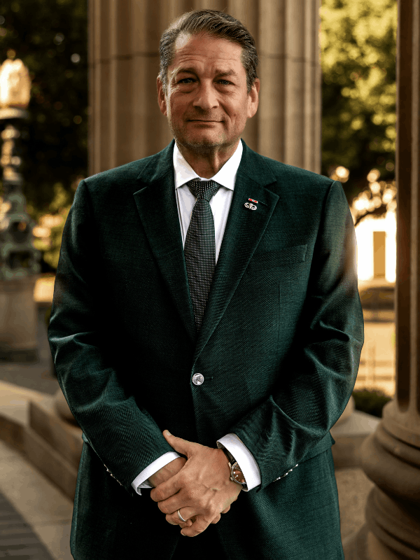 Will M. Helixon, military defense attorney, standing in a dark green suit in front of courthouse columns