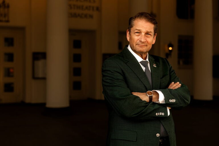 Will M. Helixon standing with arms crossed in front of a building entrance in Wiesbaden, Germany.