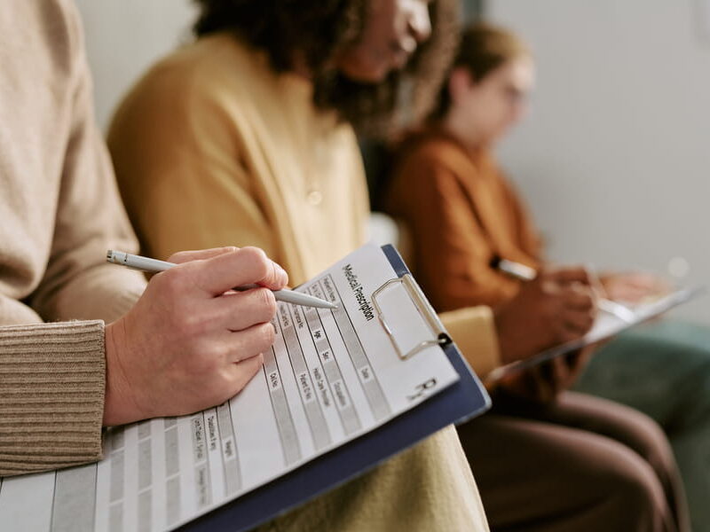 People seated in a clinic waiting room completing mental health evaluation forms