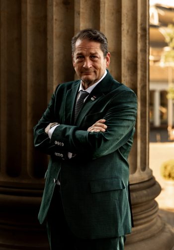 Will M. Helixon, military lawyer in green suit standing by stone columns in Wiesbaden, Germany